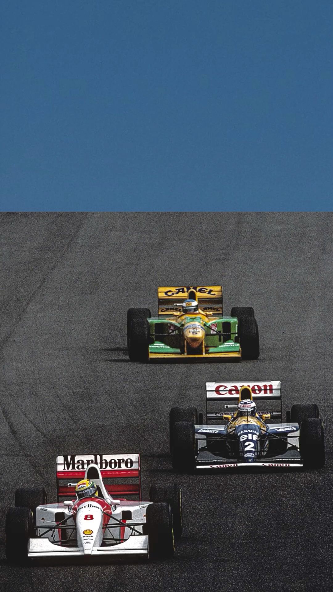 Three vintage Formula 1 cars on a racetrack with a clear blue sky.