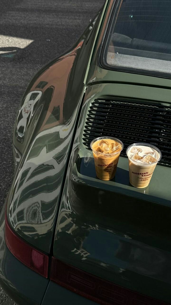 Two coffee cups on a car's open sunroof with a reflective surface.