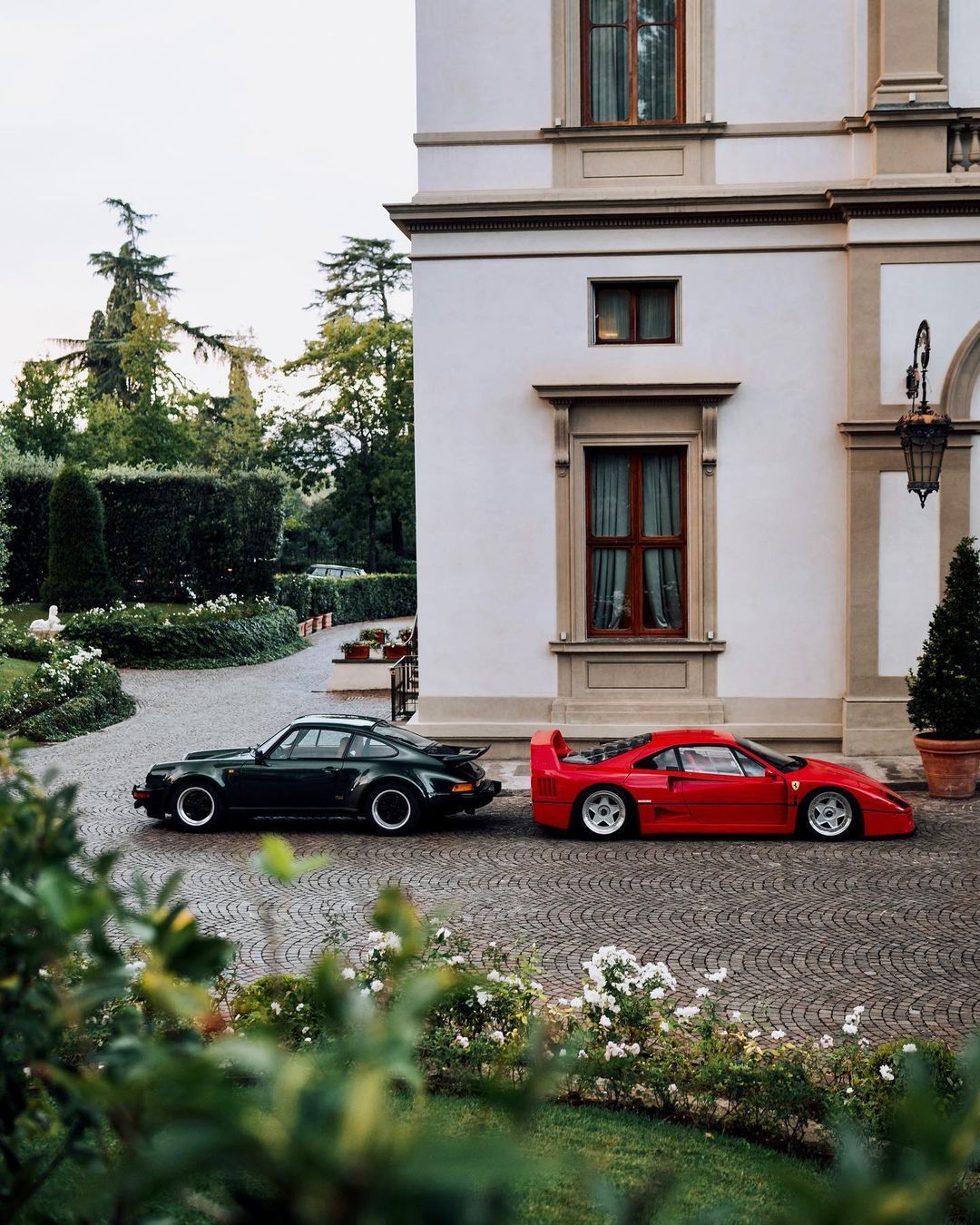 Two sports cars, one black and one red, parked in front of a classical building.
